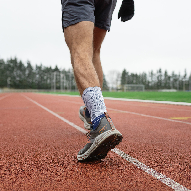 Close-up of a male runner's legs wearing blue running shoes and compression socks on a red running track.