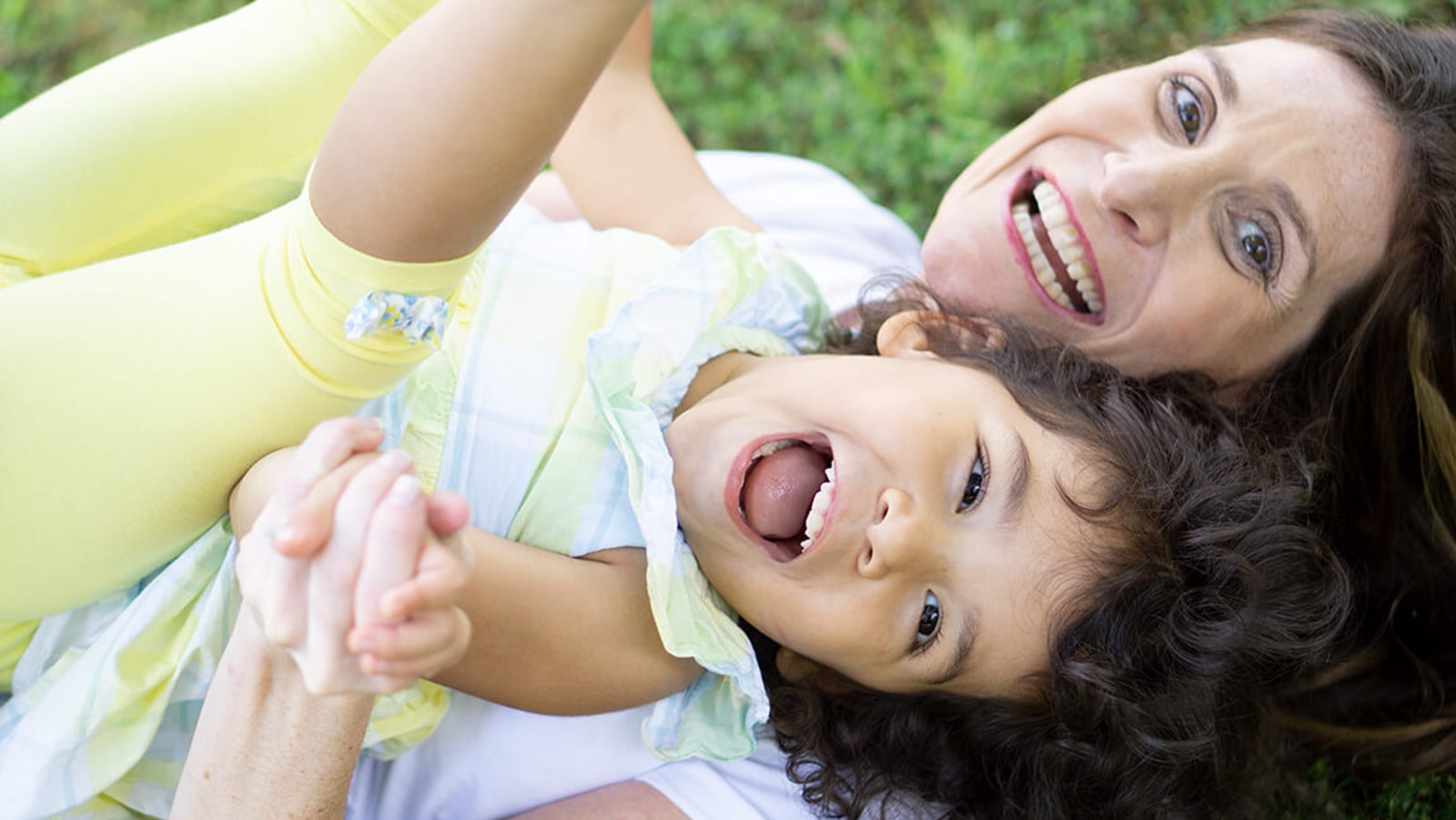 Mother and daughter playing and laughing together on grass, capturing a joyful moment outdoors.