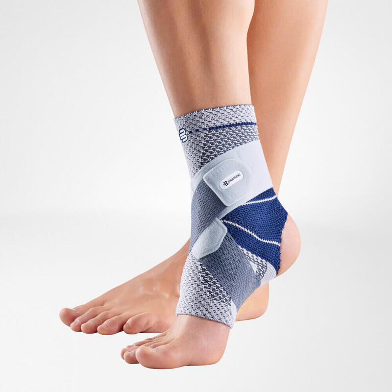 Close-up of a person wearing a blue and gray Bauerfeind ankle brace on their left foot, designed to provide support and stability.