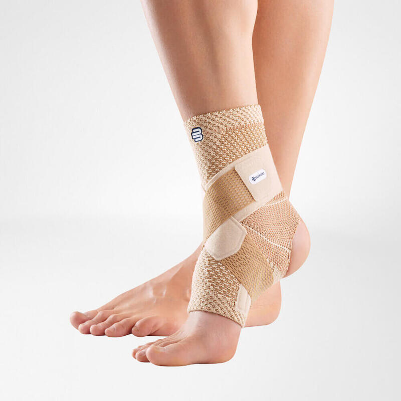 Close-up of a beige ankle support brace on a human leg, showcasing its adjustable straps and breathable fabric design against a plain light background.