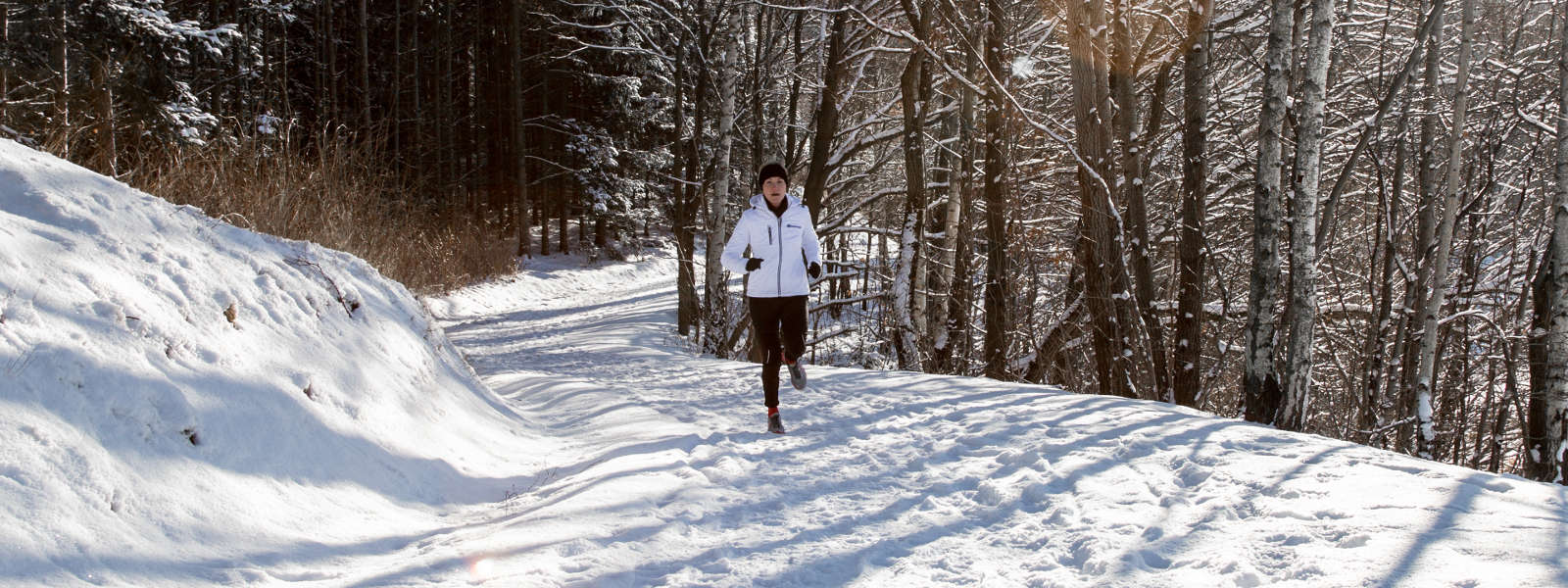 Woman running uphill through snowy weather while wearing cold weather gear and Bauerfeind's Run Performance Compression Socks.