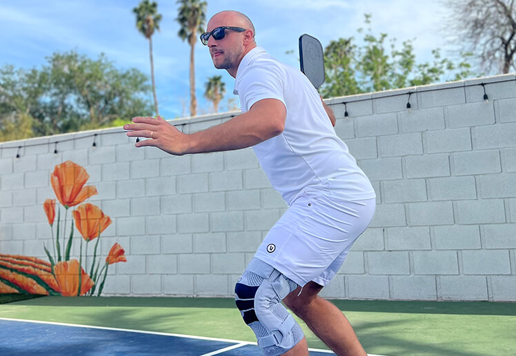 Man wearing Bauerfeind's GenuTrain S knee brace while playing pickleball outdoors.