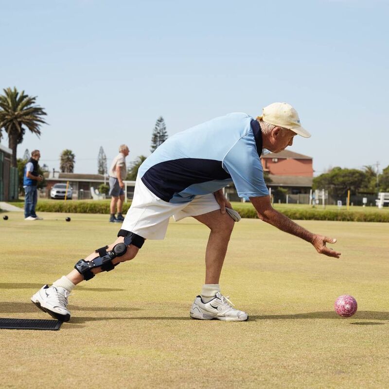 Senior man with knee brace playing lawn bowls on a sunny day.