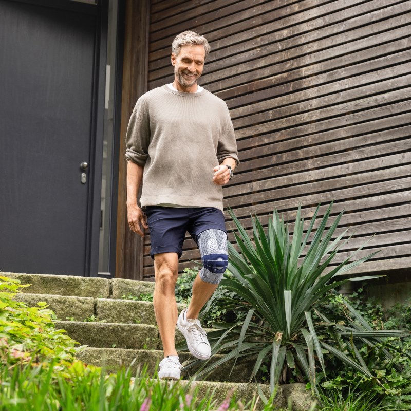 Man leaving his house by walking down steps wearing Bauerfeind's GenuTrain A3 arthritis knee brace.