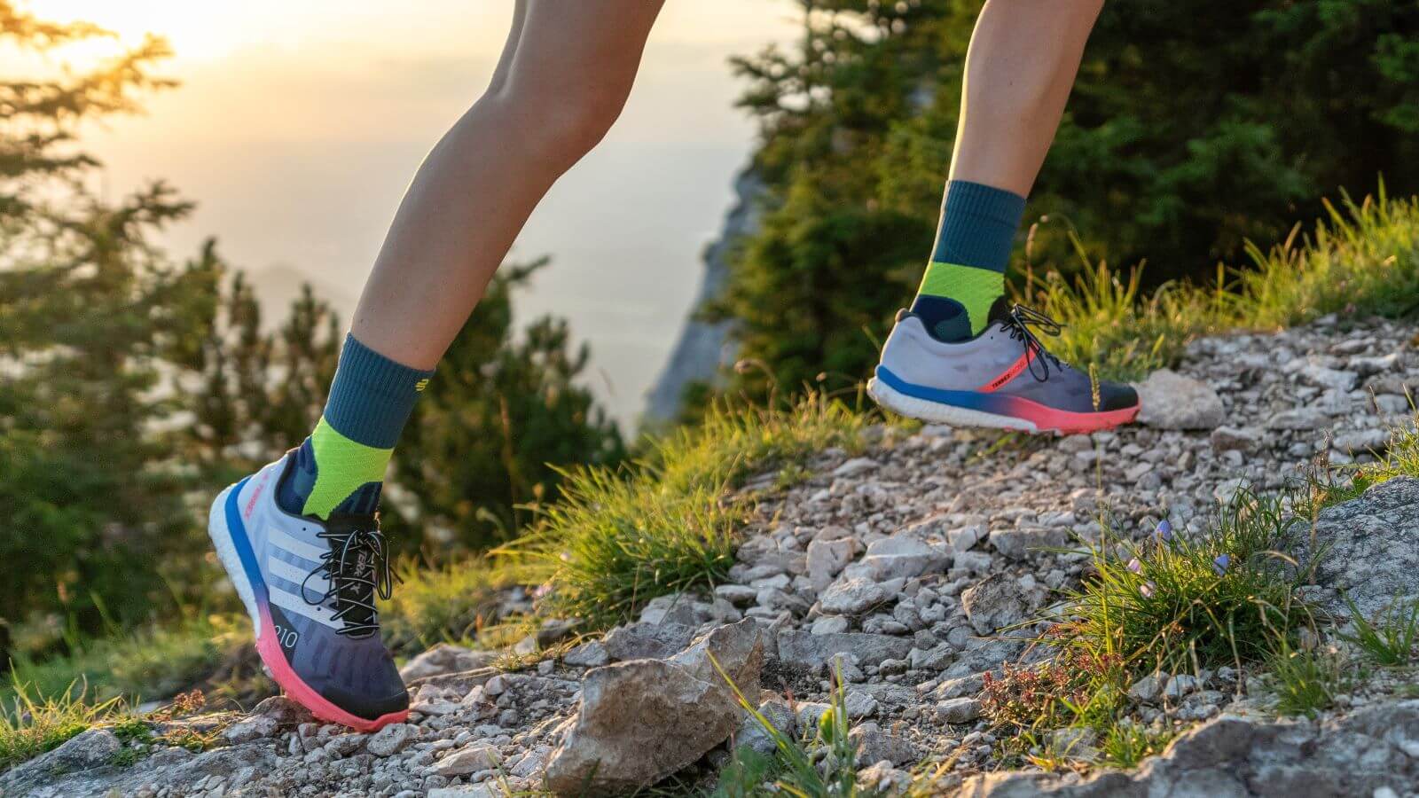 Close-up image of a person wearing Bauerfeind's Trail Run Mid Cut Socks while running uphill on a gravel trail through the forest.