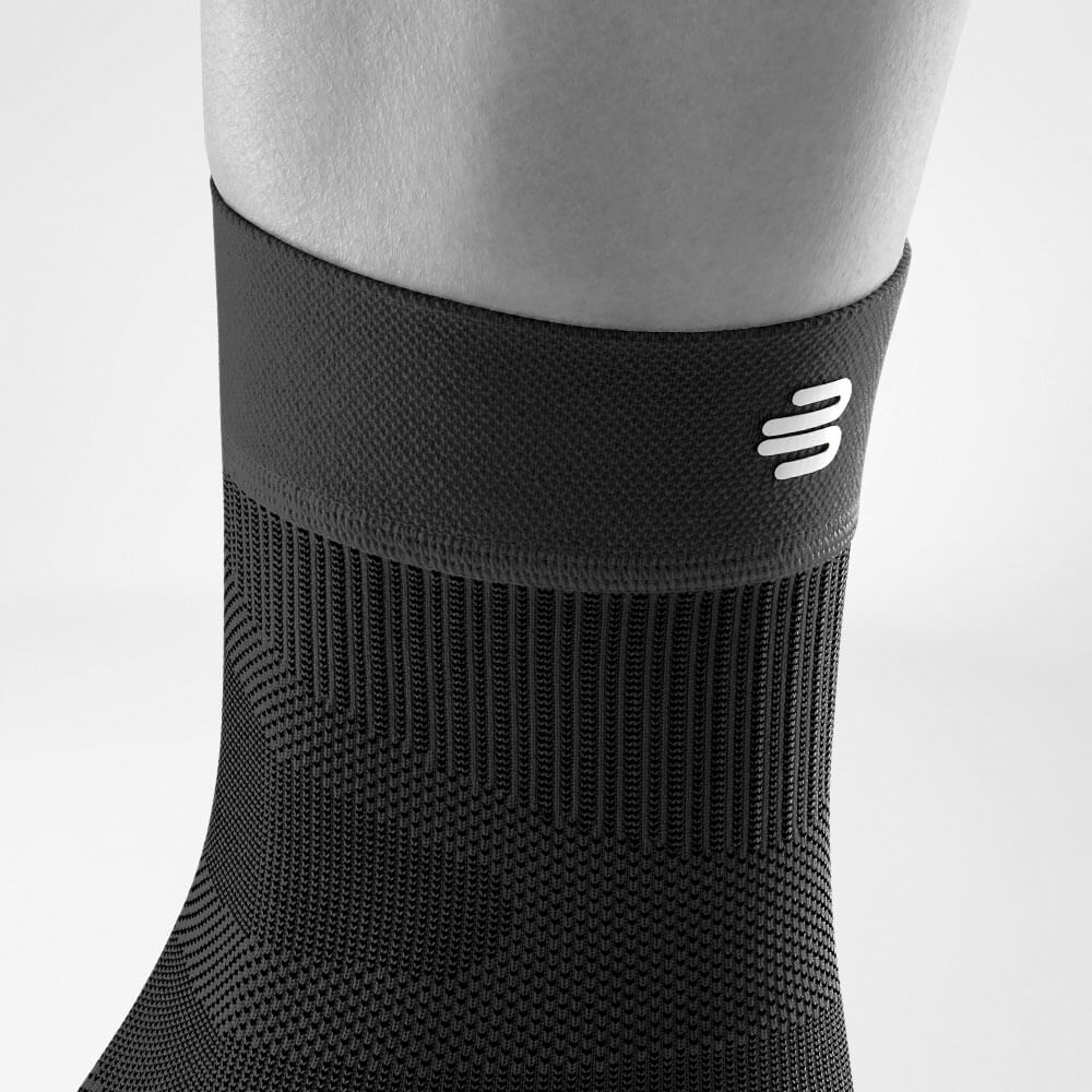 Close-up of a black compression sock with white logo on a person's leg, highlighting the texture and fit.