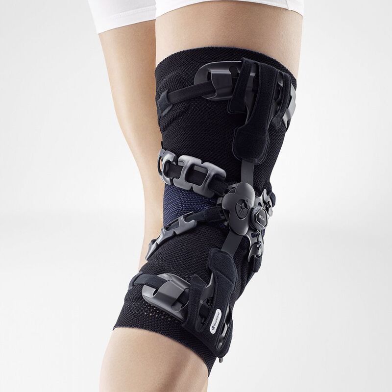 Close-up of a person adjusting a modern black knee brace with straps and orthopedic support on their left knee.