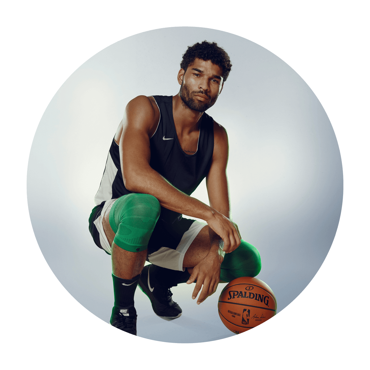 Athlete bending down near a basketball while wearing Bauerfeind's Sports Compression Knee Support NBA Celtics Edition.