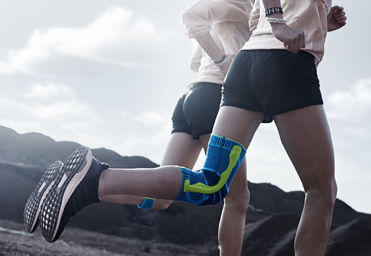 Two women running while one wears Bauerfeind's Sports Knee Support and the other wears Bauerfeind's Sports Knee Strap.