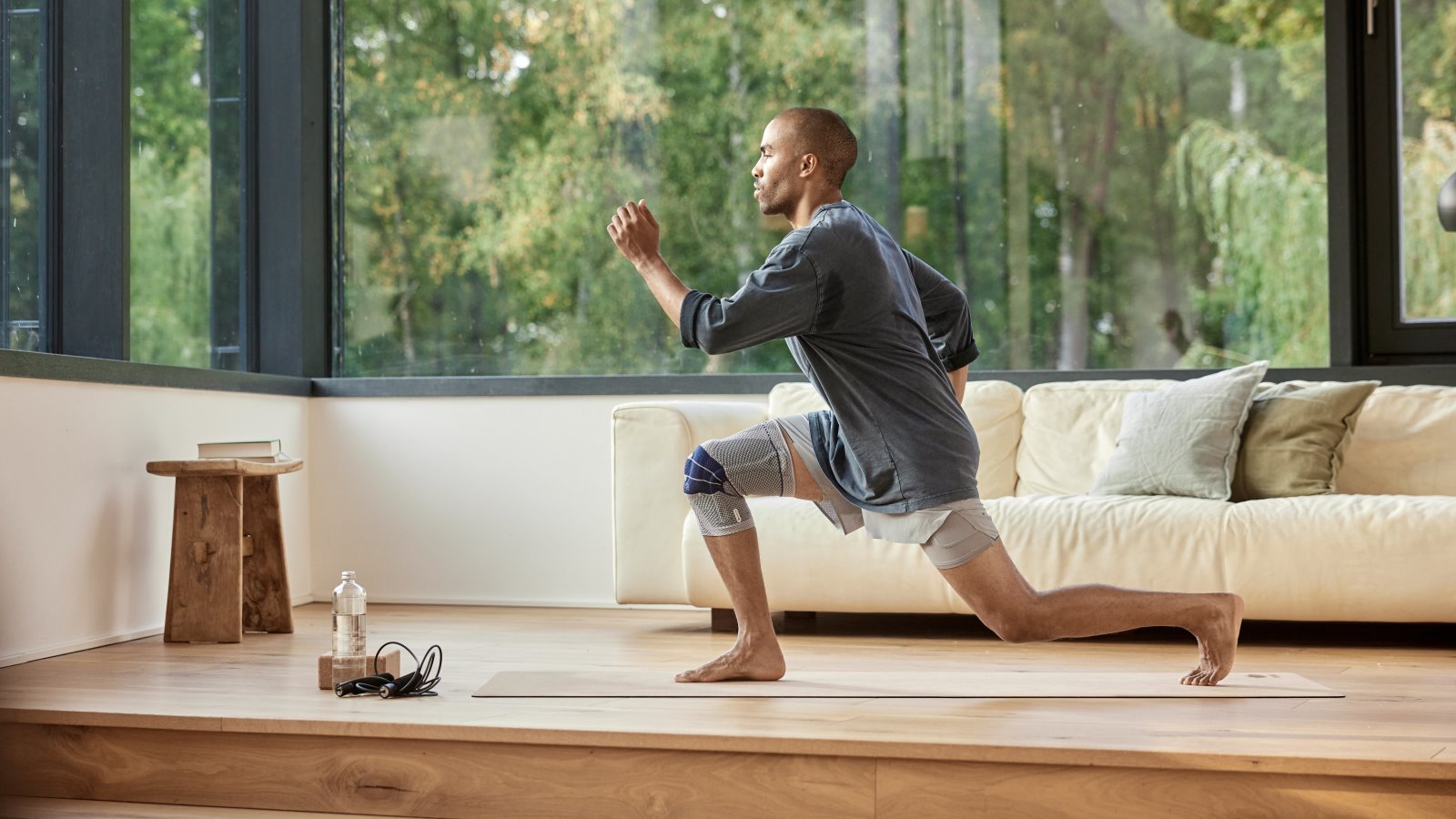 Man performing lunges during an in-home workout while wearing Bauerfeind's GenuTrain knee brace.