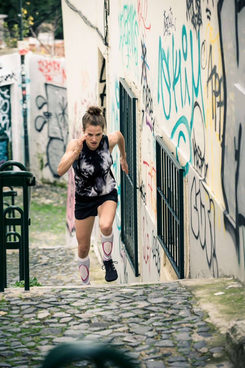 Woman wearing Bauerfeind's Run Performance Compression Socks while running through a city street.