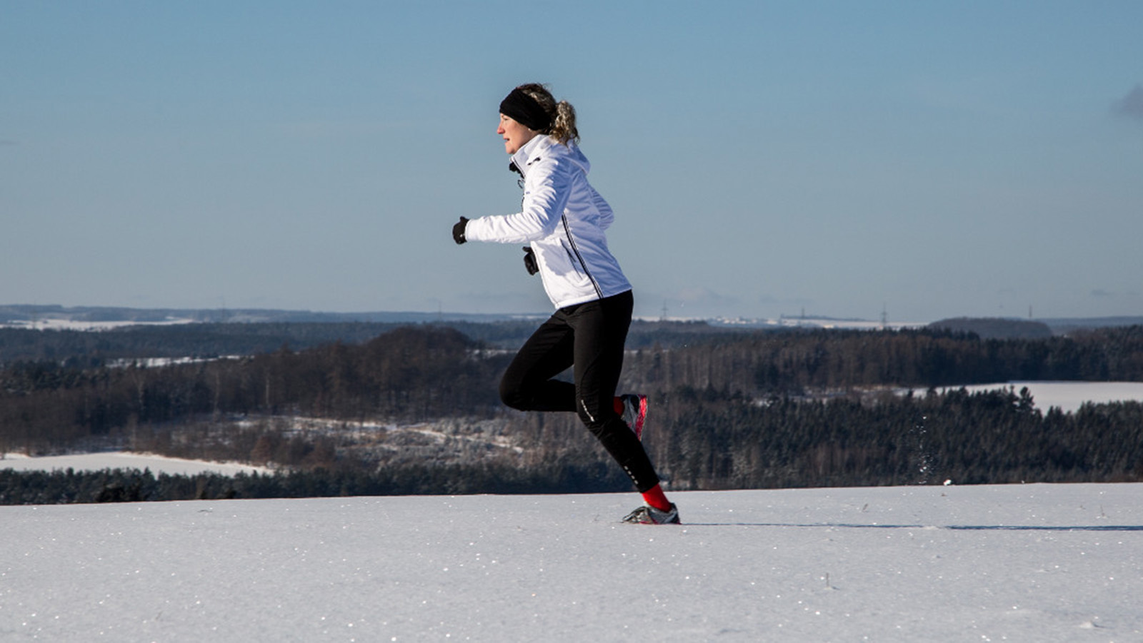 Woman adjusting the hood of her jacket before running in snowy weather. 