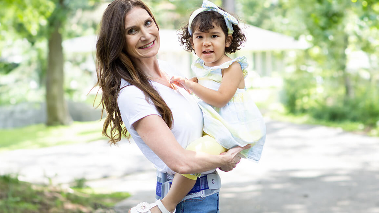 Smiling mother holding her child while wearing Bauerfeind's SacroLoc SI joint belt.