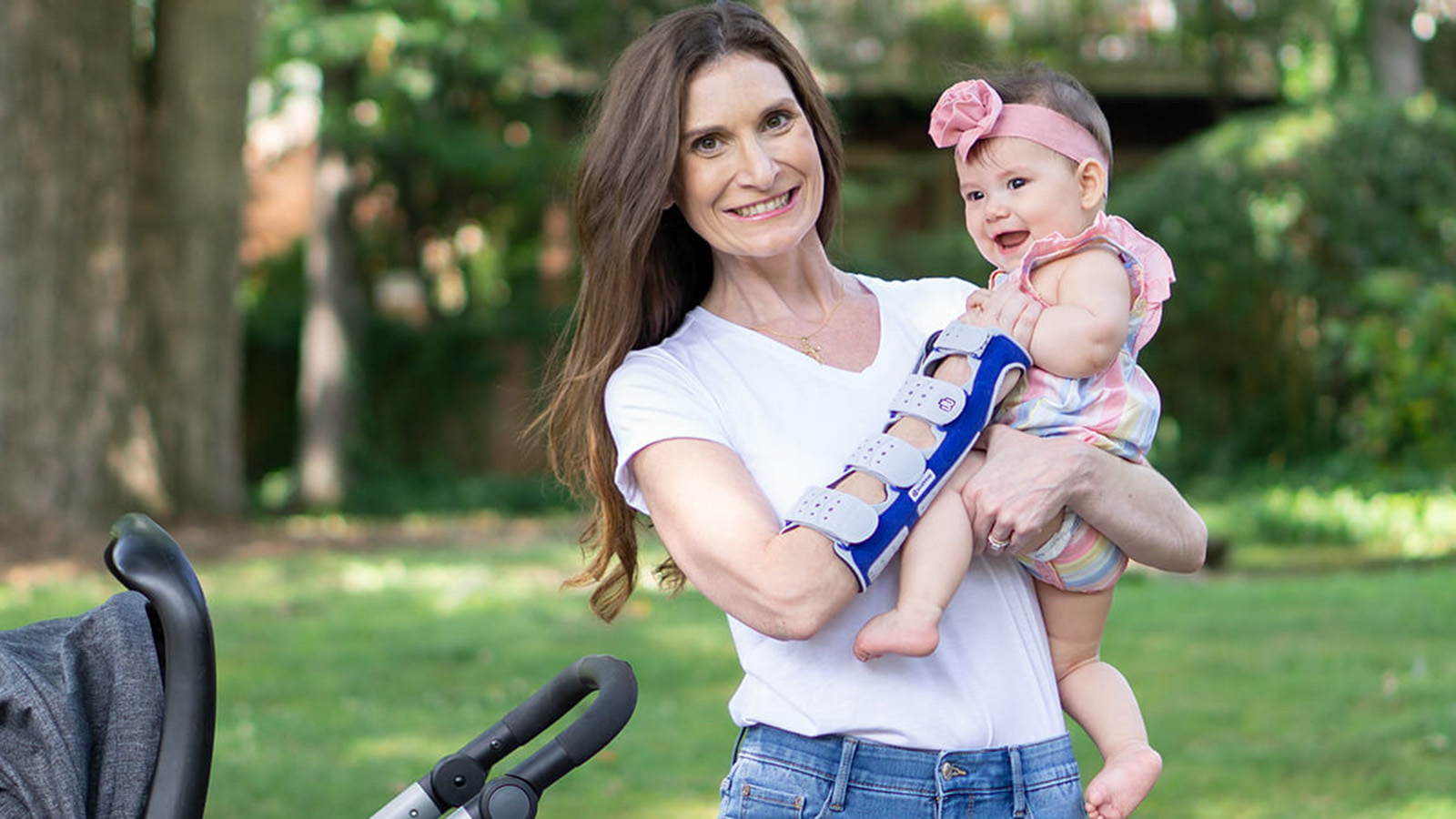 Smiling mother holding her child while wearing Bauerfeind's SacroLoc SI joint belt.