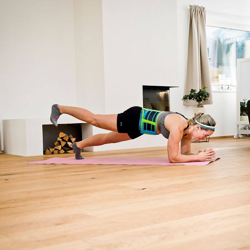 Woman performing the plank exercise while at home wearing Bauerfeind's Sports Back Support.