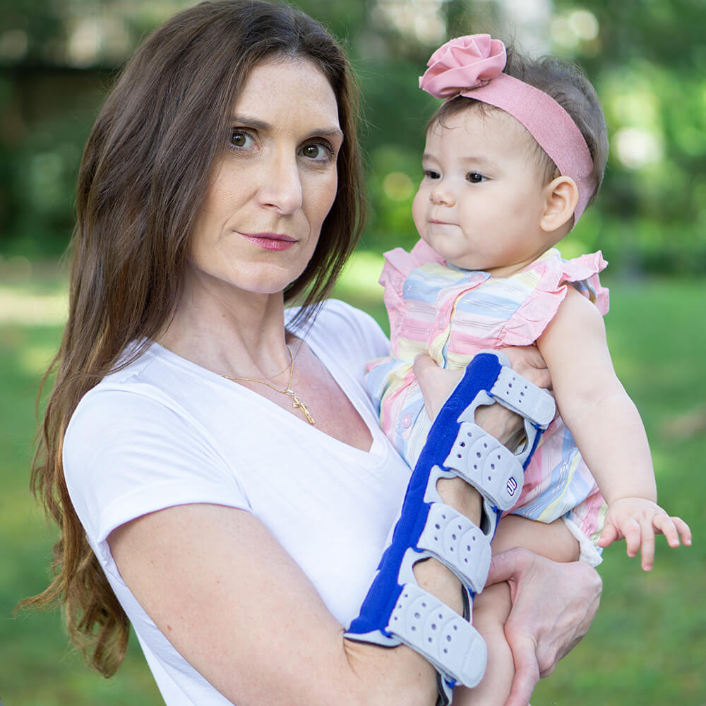 Mother holding her baby while wearing Bauerfeind's ManuLoc long wrist brace.