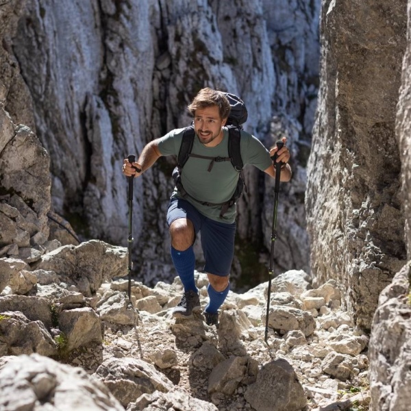 Man trekking up rocky mountain terrain while wearing Bauerfeind's Outdoor Merino Compression Socks.