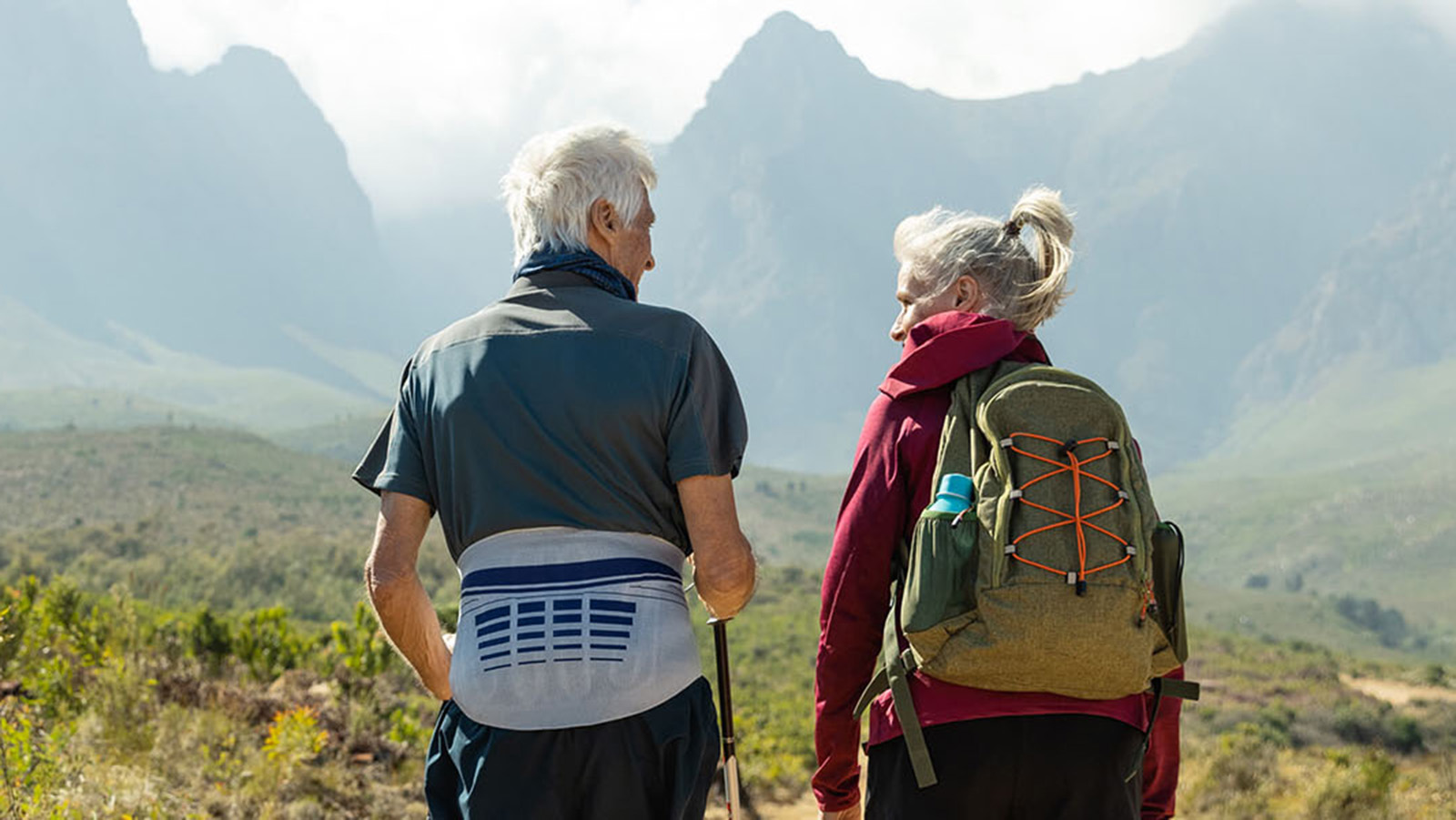 Senior man wearing Bauerfeind's LumboLoc back brace while hiking with a senior woman.