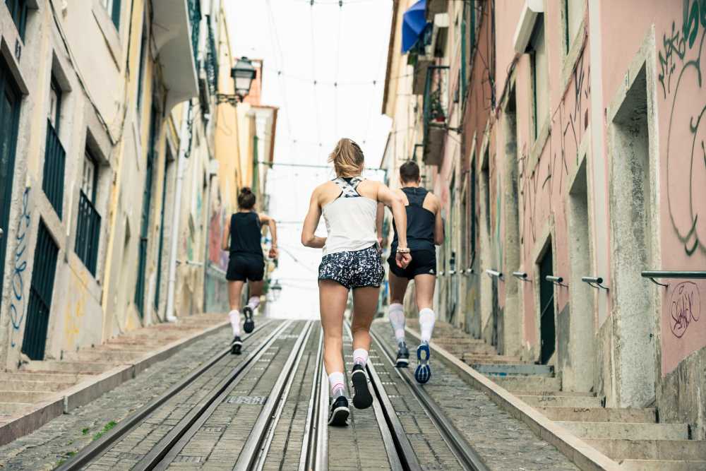 Three young adults wearing Bauerfeind's Run Performance Compression Socks while running uphill in an inner-city street.