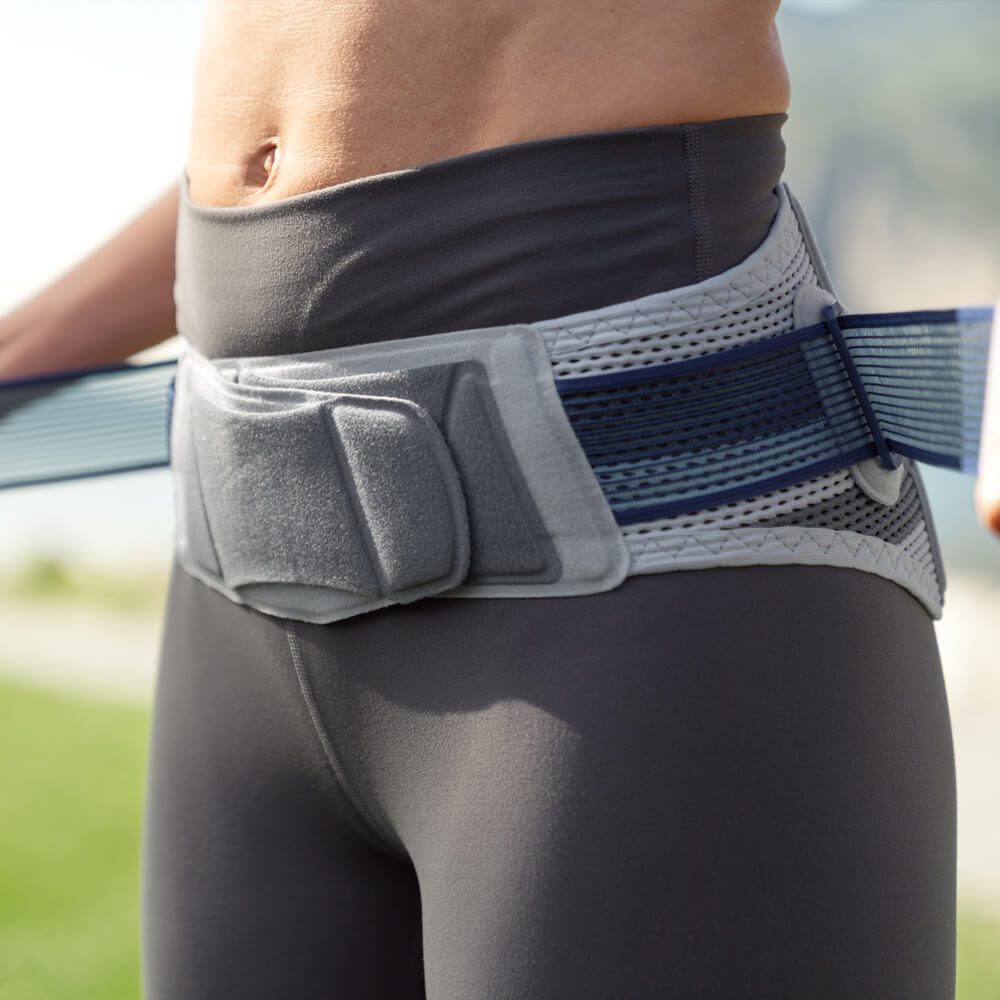 Close-up of a person adjusting the tension straps of Bauerfeind's SacroLoc SI joint belt before practicing yoga outdoors.