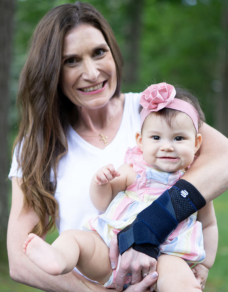 Smiling mother carrying her child during a walk outside while wearing Bauerfeind's ManuTrain wrist brace.