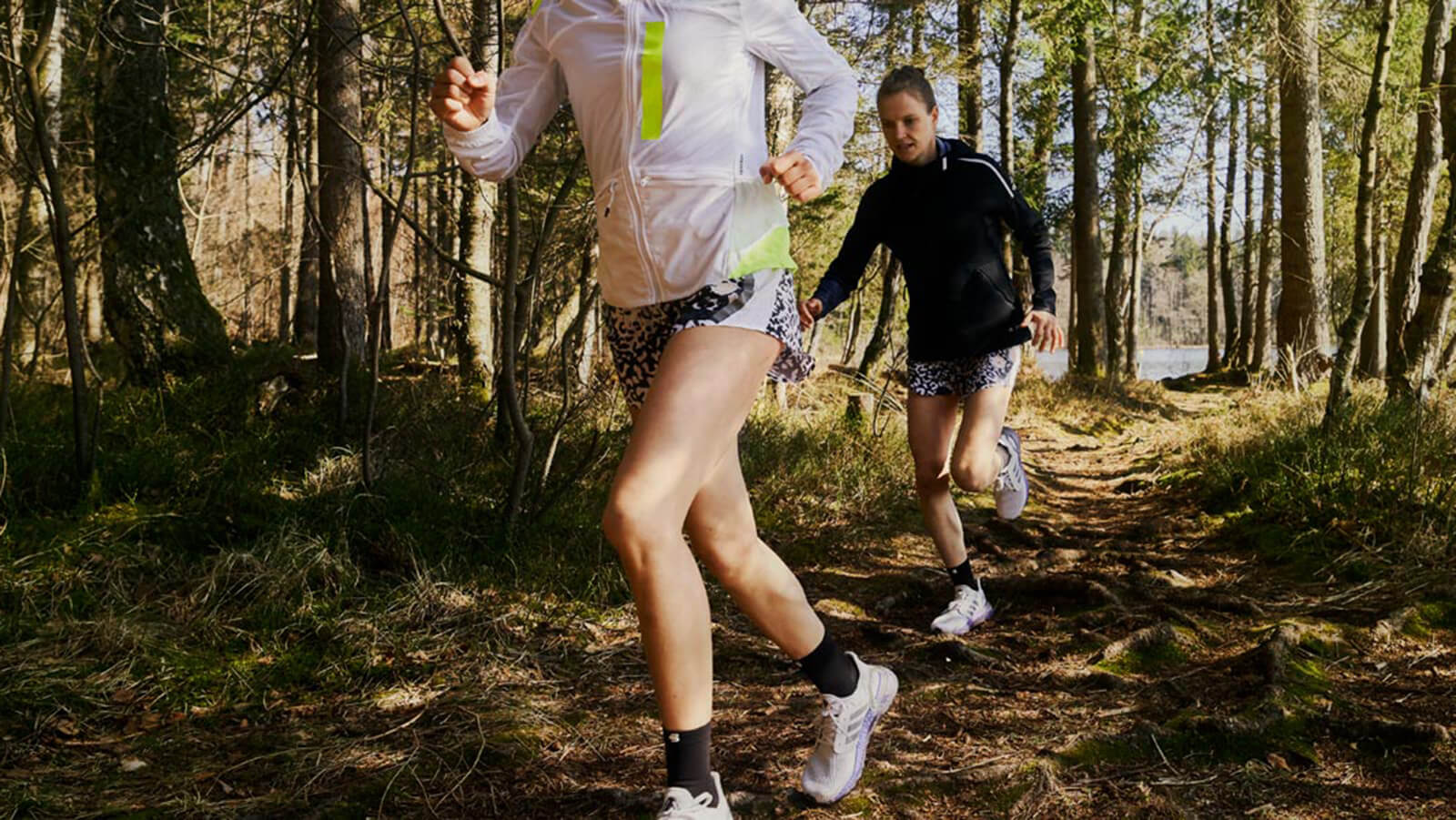 Two women running through a forest trail in the morning.