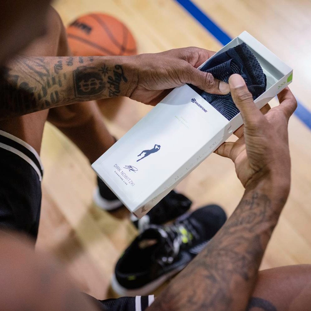 Close-up of a basketball player holding a box of Dirk Nowitzki sport socks on a basketball court.