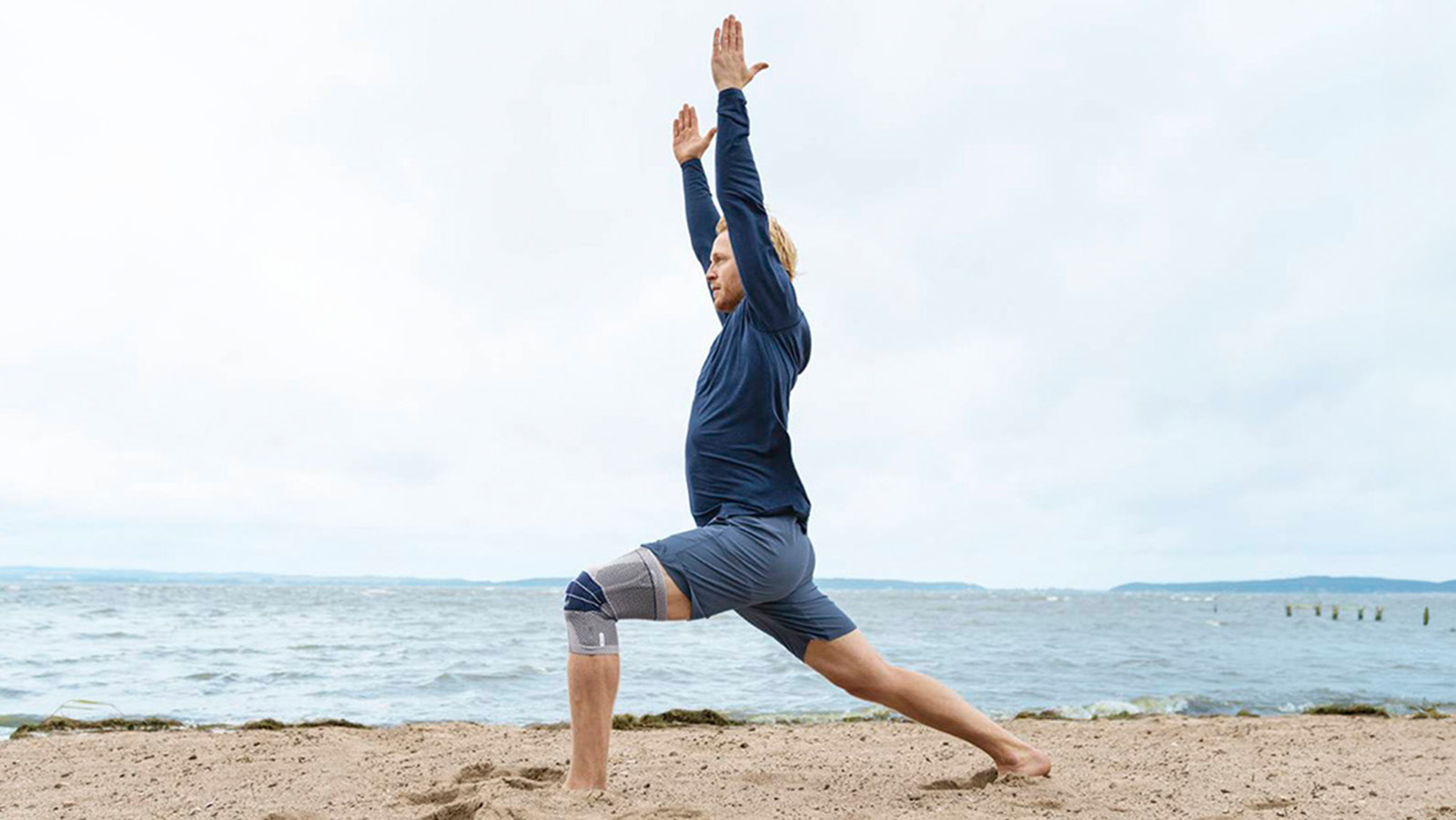 Man practicing yoga while wearing Bauerfeind's GenuTrain knee brace on the beach.