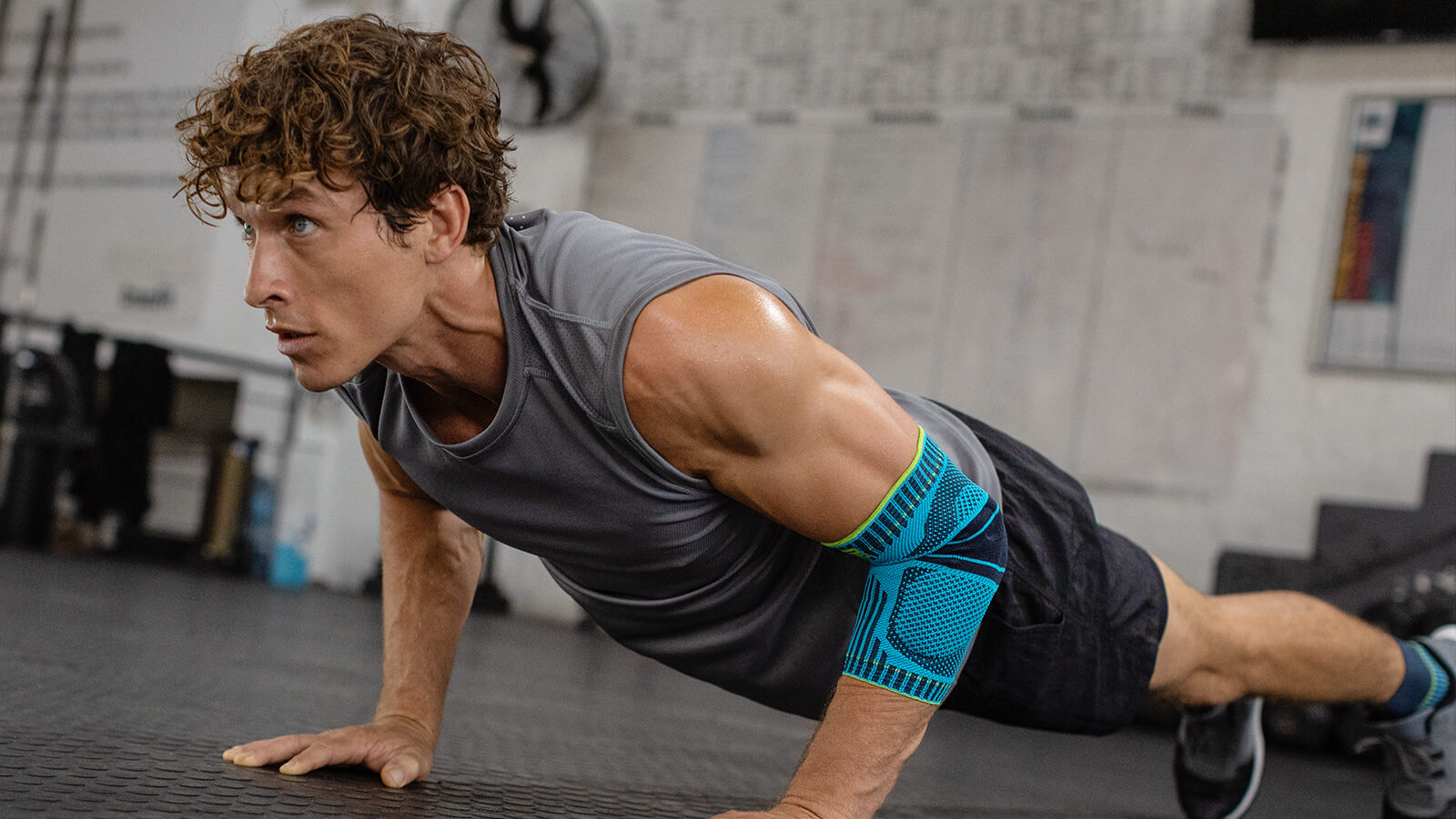 Man performing push-ups in the gym while wearing Bauerfeind's Sports Elbow Support.