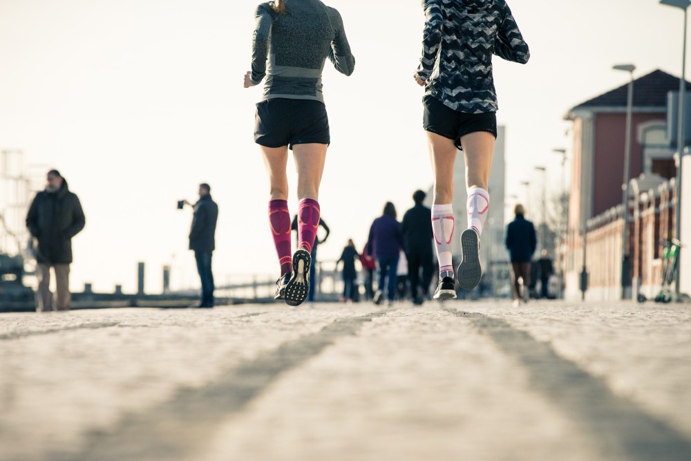 Woman wearing Bauerfeind's Run Performance Compression Socks while running through a city street.