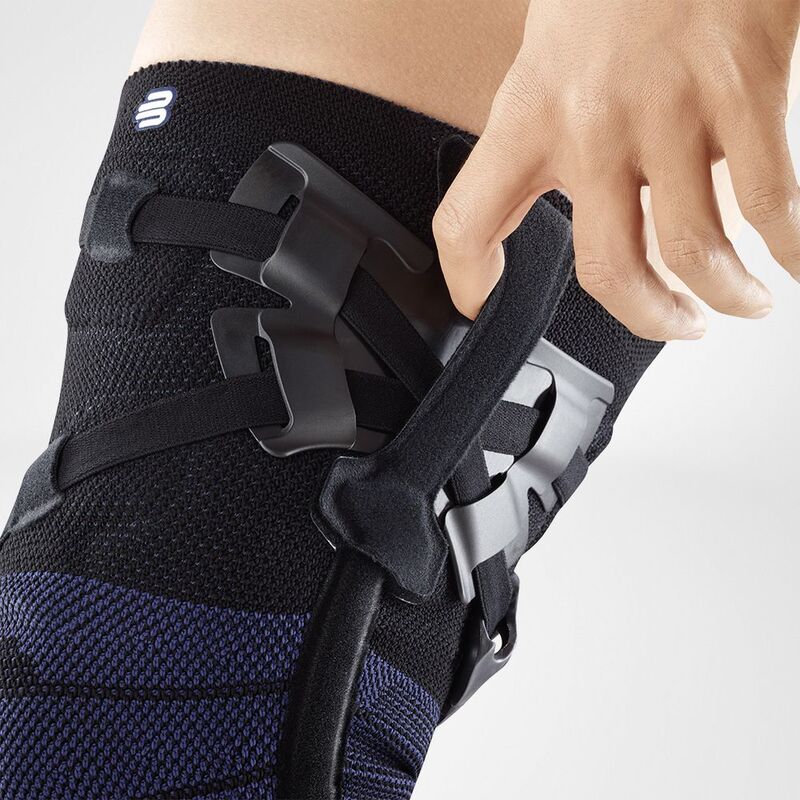 Close-up of a person adjusting a modern black knee brace with straps and orthopedic support on their left knee.