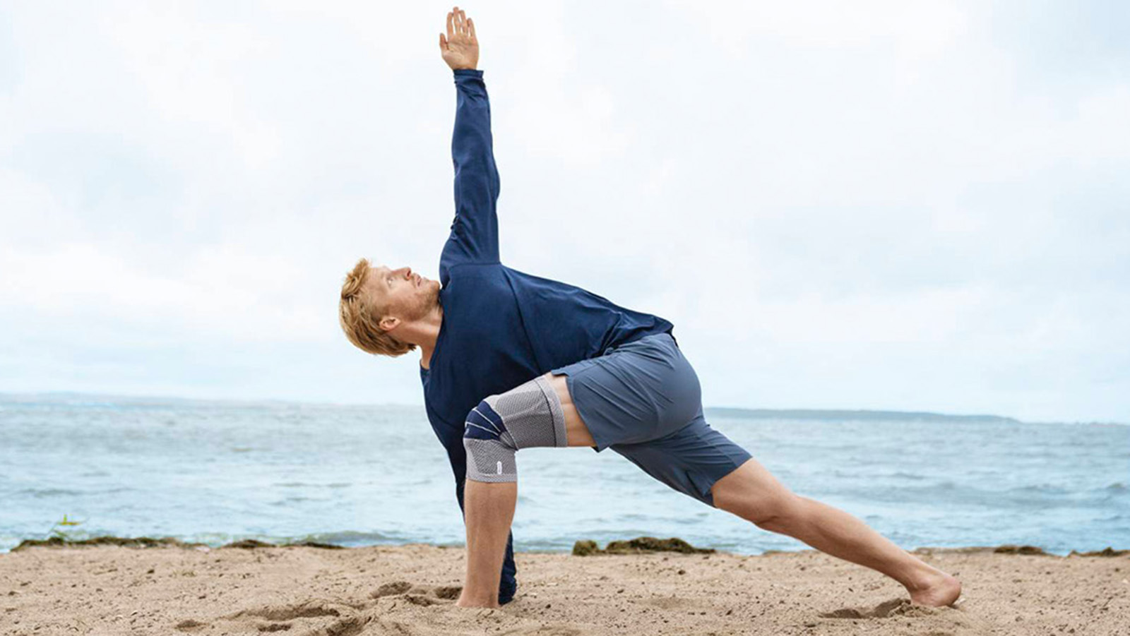 Man practicing yoga while wearing Bauerfeind's GenuTrain knee brace on the beach.