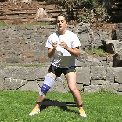 Young woman performing the banded side shuffle exercise in her back yard while wearing Bauerfeind's GenuTrain knee brace.