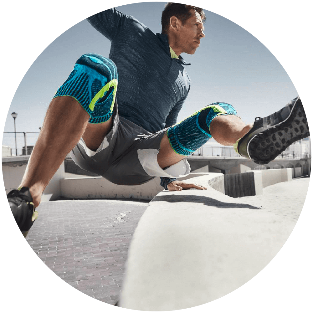 Man jumping over a concrete wall while wearing Bauerfeind's Sports Knee Support.