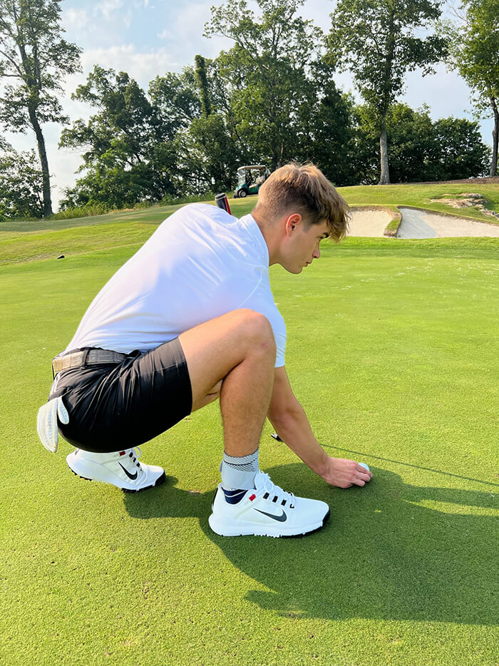 Golfer bending down to read putt while wearing Bauerfeind's MalleoTrain Plus ankle brace.