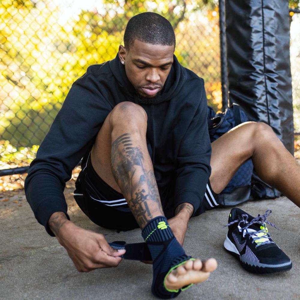 Basketball player wearing black sneakers and colorful socks sitting on an outdoor court with a ball