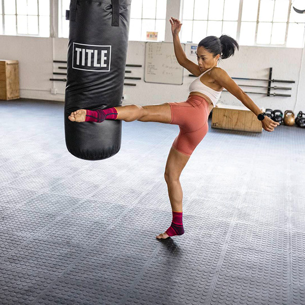 Woman wearing Bauerfeind's Sports Back Support while performing a rope exercise in an indoor gym.