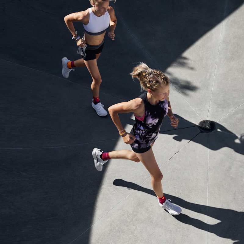 Two women running outside while wearing Bauerfeind's Sports Ankle Support.