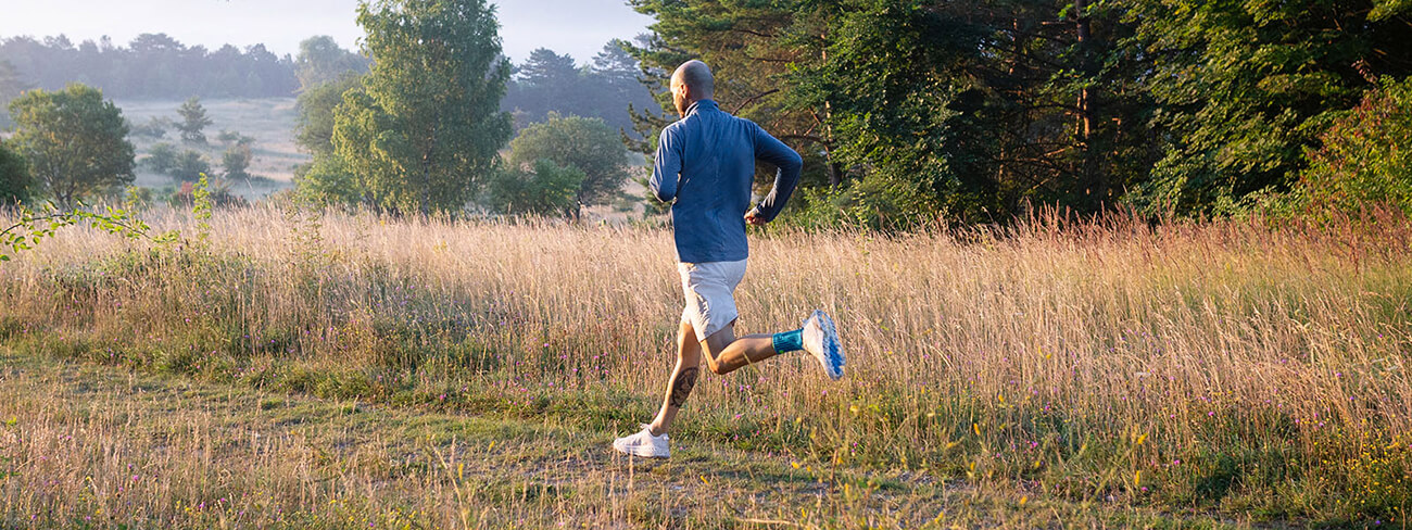 Man wearing Bauerfeind's Sports Achilles Support while on a morning run through a grassy field.