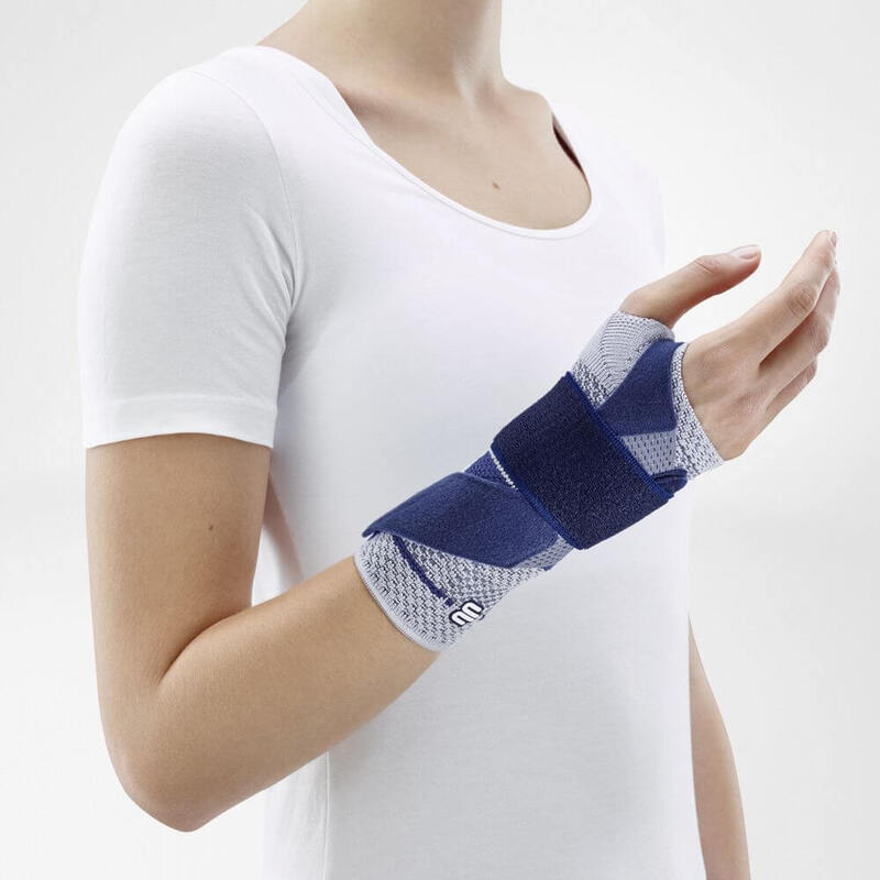 Woman wearing Bauerfeind's ManuTrain wrist brace (titan) while standing in front of a gray background.