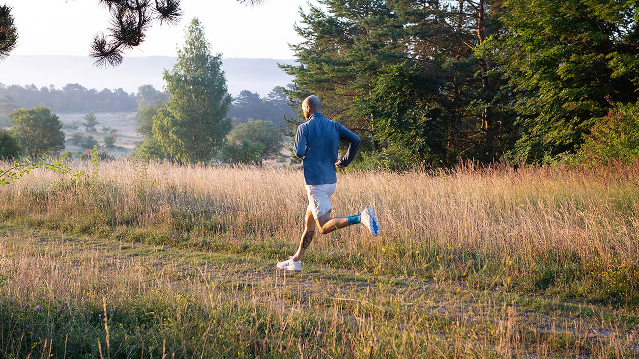 Man wearing Bauerfeind's Sports Achilles Support while on a morning run through a grassy field.