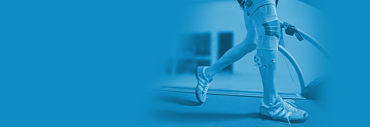 Person with prosthetic legs walking on a treadmill in a rehabilitation center, highlighted in blue tones.