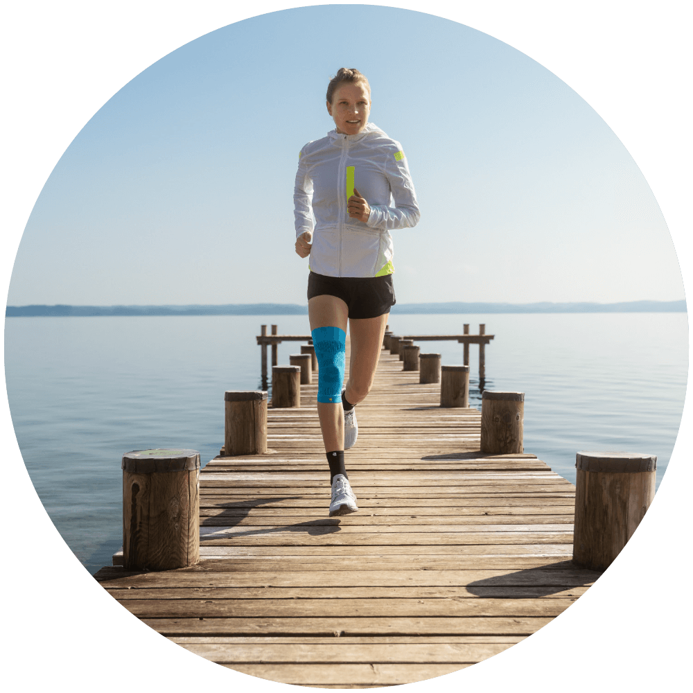 Woman running on a dock surrounding by a lake while wearing Bauerfeind's Sports Compression Knee Support.