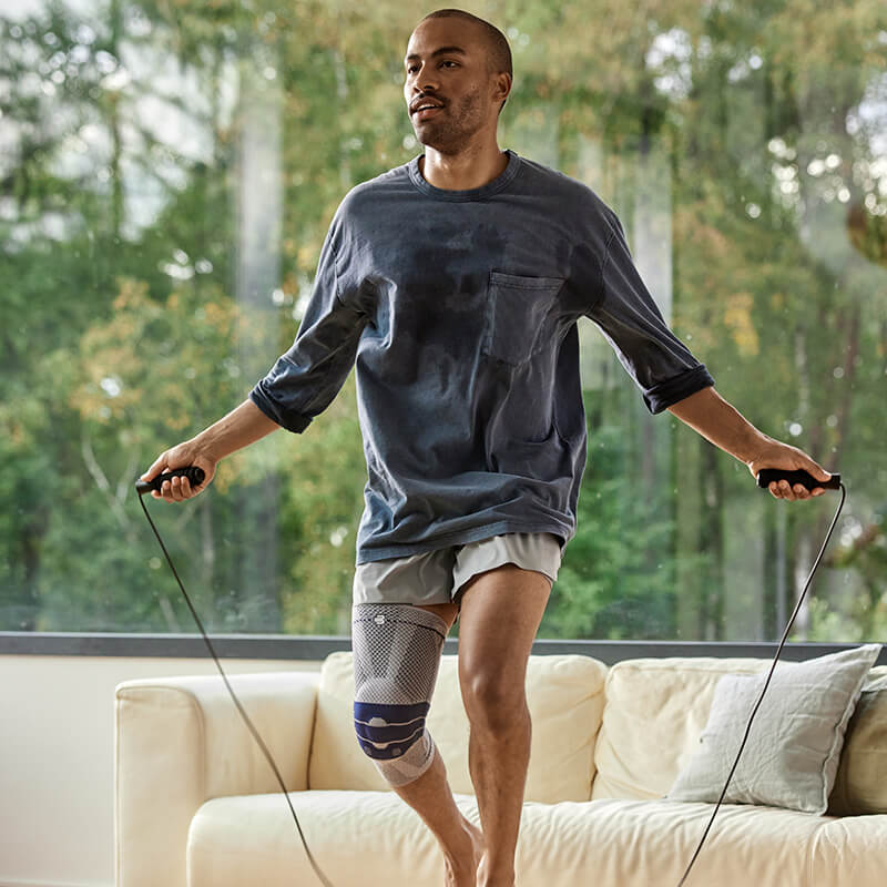 Image of a man wearing Bauerfeind's GenuTrain knee brace while jumping over a wall.