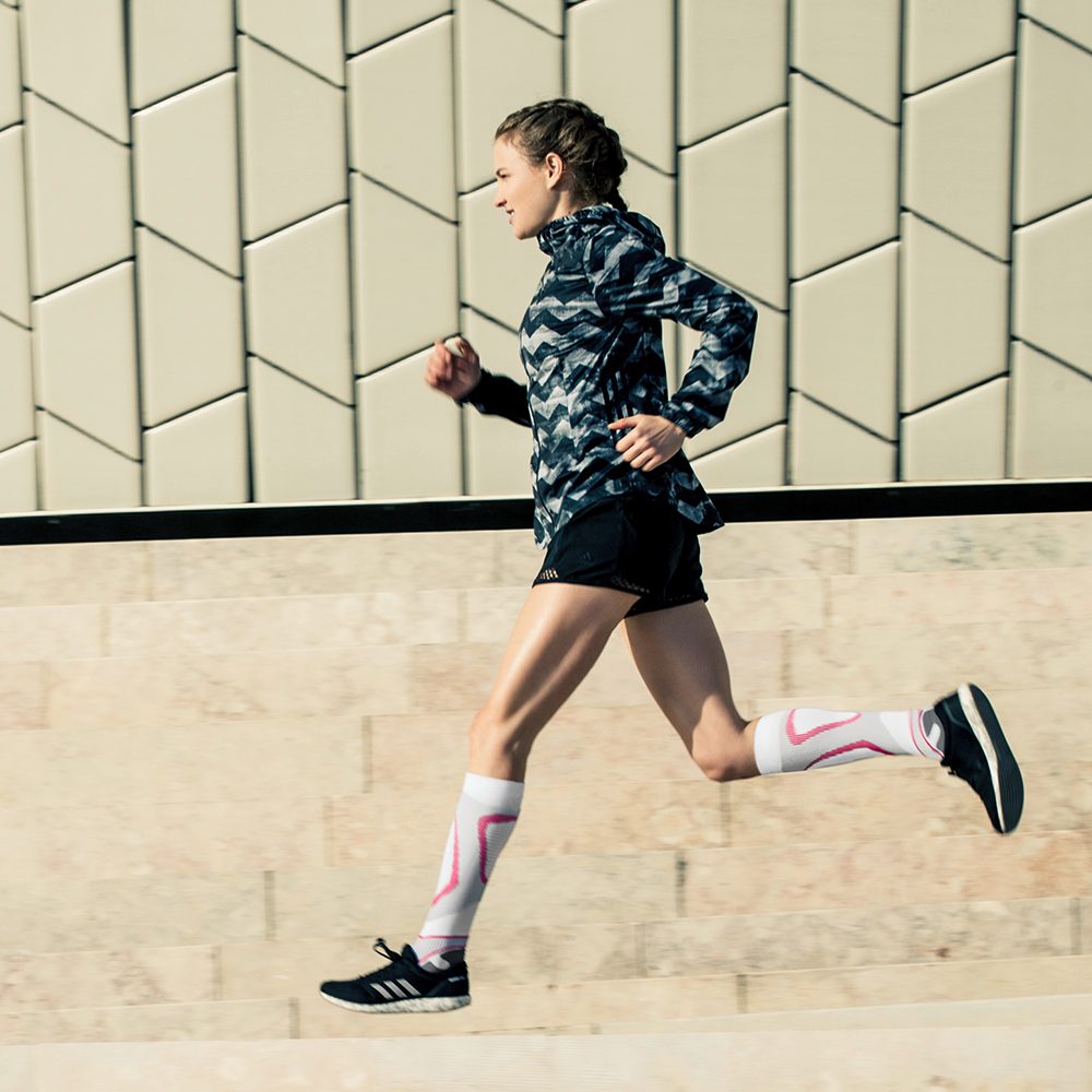 Woman wearing Bauerfeind's Run Performance Compression Socks while running through a city street.