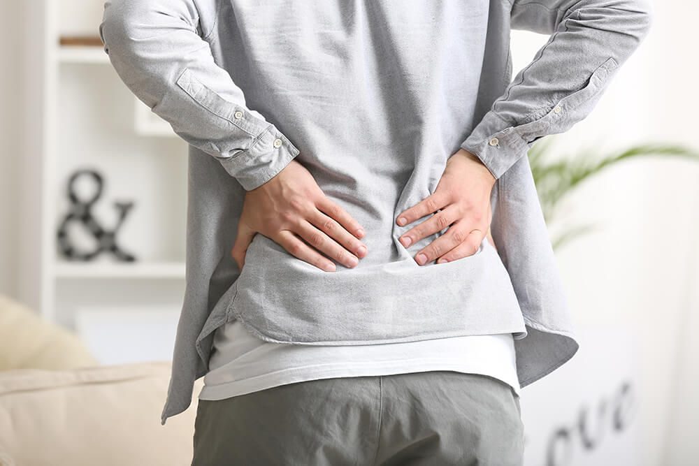 Person holding lower back in pain indicating backache or lumbar discomfort.