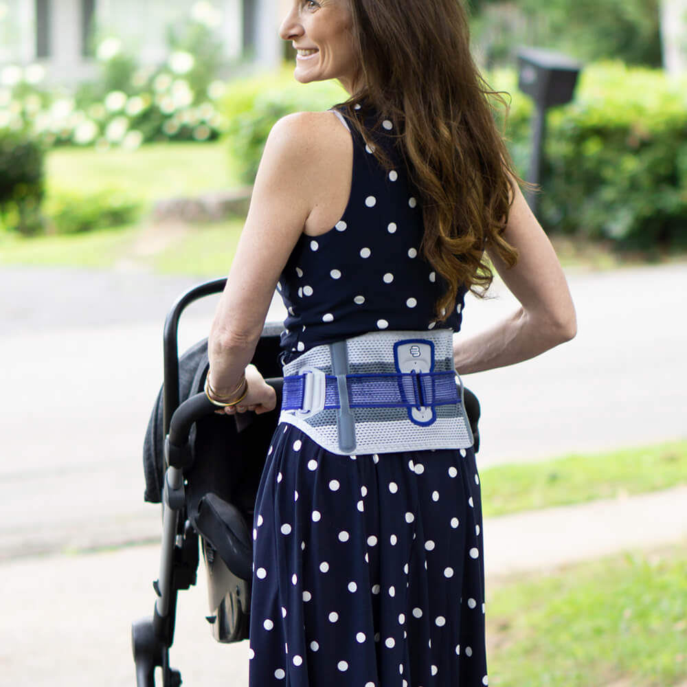 Smiling mother carrying her child during a walk outside while wearing Bauerfeind's ManuTrain wrist brace.