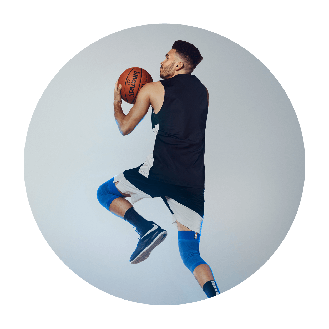 Athlete attempting a layup on an indoor basketball court while wearing Bauerfeind's Sports Compression Knee Support NBA Mavericks Edition.