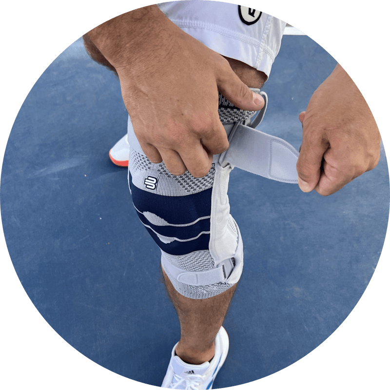 Man adjusting the circular strap system of Bauerfeind's GenuTrain S knee brace before beginning to play pickleball outdoors.