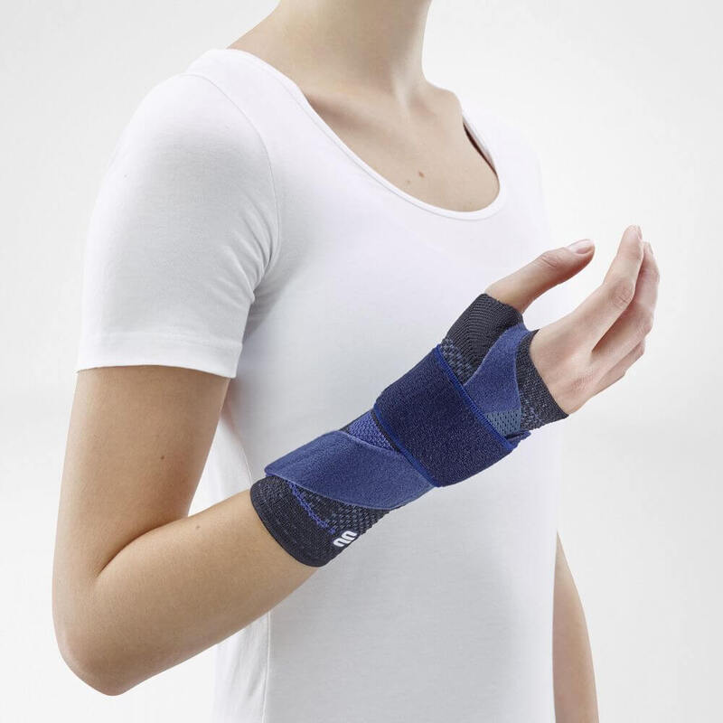 Woman wearing Bauerfeind's ManuTrain wrist brace (beige) while standing in front of a gray background.